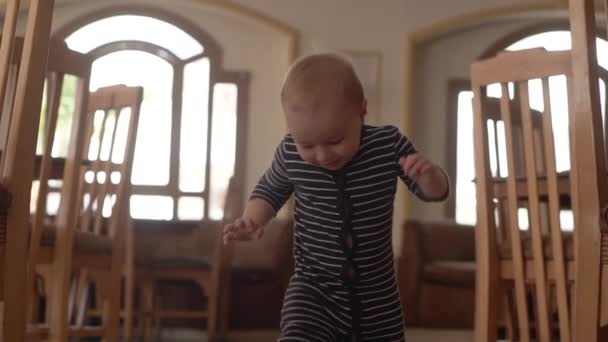 Bambino in tuta cammina sul buffet vicino a sedie di legno . — Video Stock