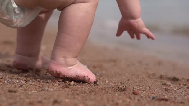小さな男の子が浜辺に座って、スローモーションで砂に触れる. — ストック動画