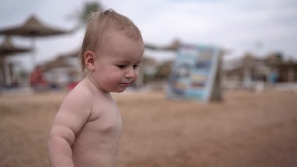 Lindo niño rubio en la playa se para y tiene buen humor . — Vídeo de stock