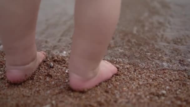 ビーチの砂の上に小さな赤ちゃんの小さな脚が立っている. — ストック動画