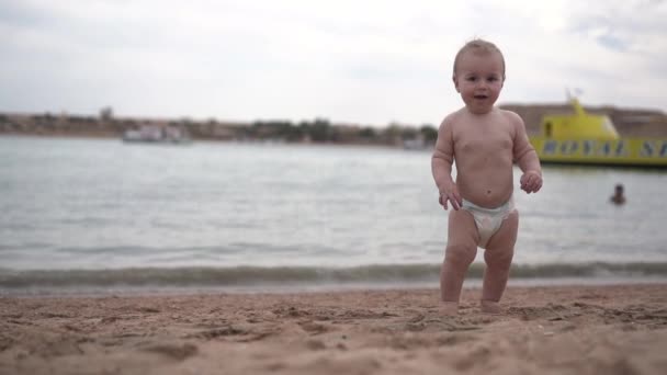 Lindo bebé se sienta en la arena en la playa que descubre este mundo . — Vídeos de Stock