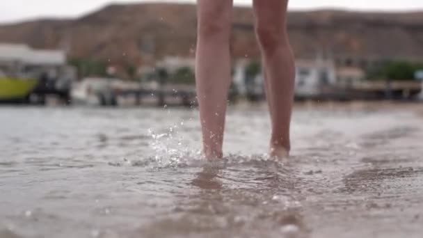 Las piernas de la mujer camina en la orilla y hace un montón de gotas en cámara lenta . — Vídeos de Stock