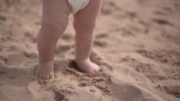 Lindas piernas pequeñas del niño pequeño se para en la arena en la playa . — Vídeos de Stock