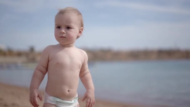 Söt blond unge med Sirious ansikte står på stranden och tittar på havet. — Stockvideo