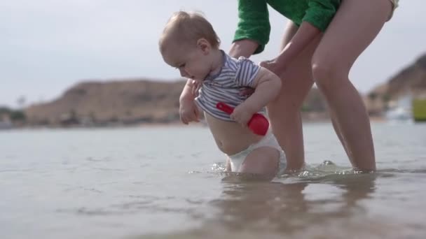 Liten unge promenad i vattnet med mamma som skyddar honom i slow motion. — Stockvideo