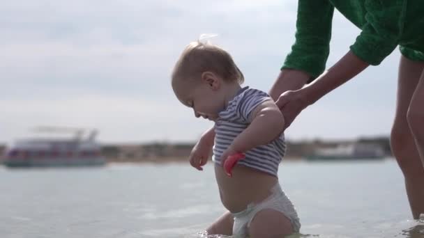 快乐的孩子和保护他慢动作的母亲一起在水中行走. — 图库视频影像