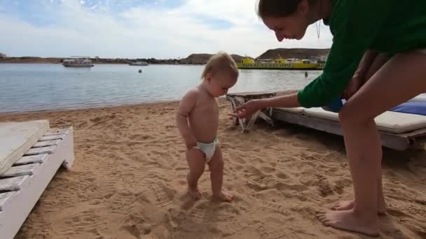 Mamá y el pequeño bebé en la playa, bebé comiendo algo — Vídeos de Stock