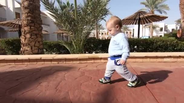 Bebê bonito caminha ao redor do território de um hotel tropical em câmera lenta — Vídeo de Stock