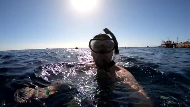 Um jovem com uma máscara mergulha debaixo da água, mostra um gesto ok, câmera lenta — Vídeo de Stock