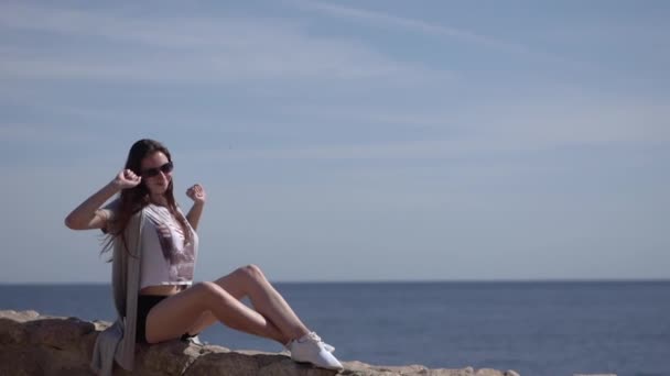 若いスレンダーガールは、石のフェンスの上に座って、彼女の手を上げます. — ストック動画