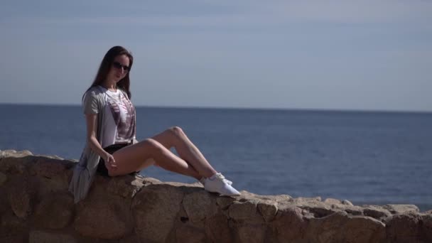 Menina senta-se na cerca na praia e dança . — Vídeo de Stock