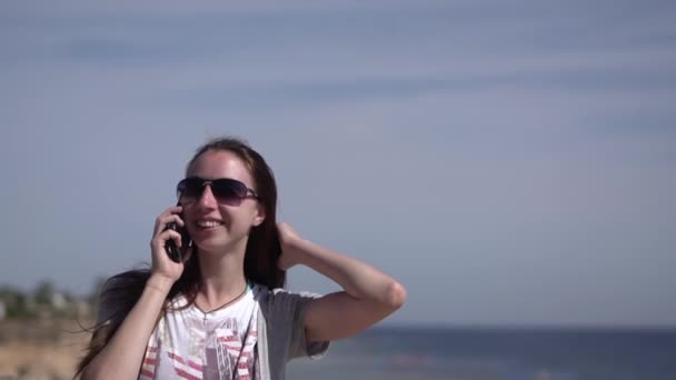 Дівчина з посмішкою розмовляє по телефону на пляжі . — стокове відео