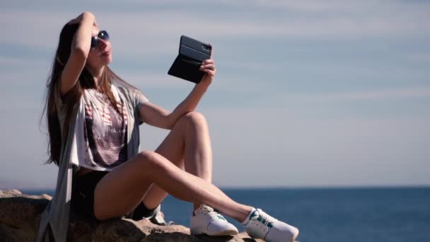 Сексуальна дівчина сидить на кам'яному паркані і робить селфі на камеру телефону  . — стокове відео