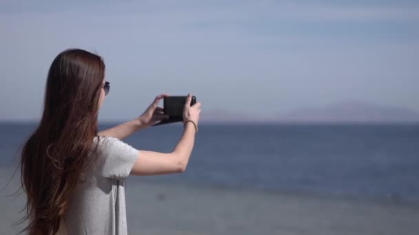 Ung flicka gör foto av havet på sin smartphone. — Stockvideo