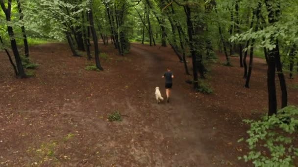 Молодой парень и белая собака бегут в листовой лесу летом — стоковое видео