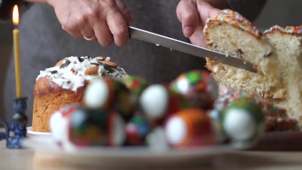 Womans hand cuts a festive Easter on the kitchen table next to a church candle. — Stock Video