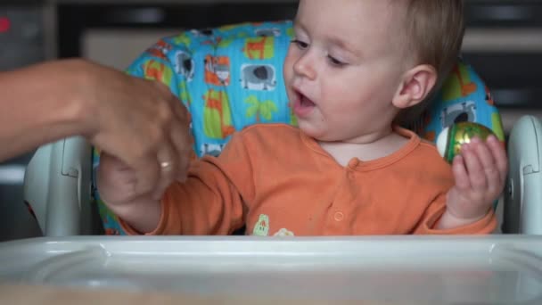 Een jaar oude baby zit in de keuken en speelt met een paasei-Slow Motion — Stockvideo