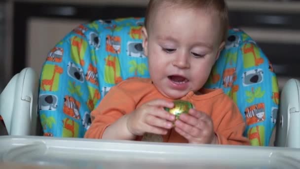One year old baby sits in the kitchen and plays with an easter egg - slow motion