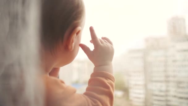 Egy kis szőke fiú áll az ablakpárkányon, és úgy néz ki az ablakon — Stock videók