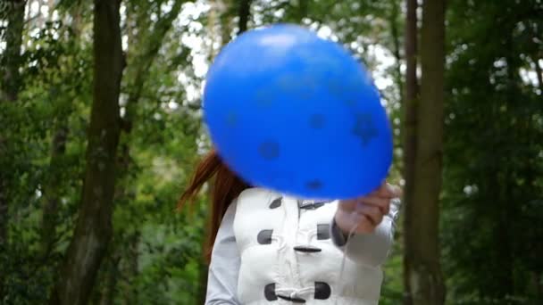 Счастливая женщина, стоящая и играющая с голубым шариком в лесу в сло-мо — стоковое видео