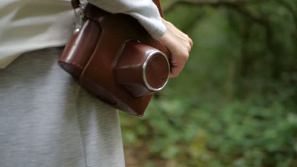 Jeune femme gardant une caméra dans un étui brun sur son épaule dans une forêt — Video