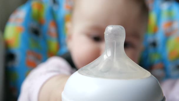 Hermoso bebé sentado y extendiendo sus manos a un biberón con leche — Vídeo de stock