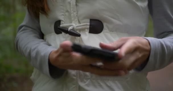 若い女性は春に森の中で情報を求めるために彼女のスマートフォンを開く — ストック動画