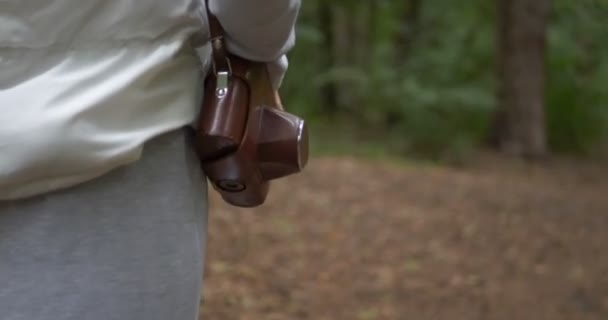 Стройная женщина держит камеру в коричневом футляре на плече в лесу весной — стоковое видео