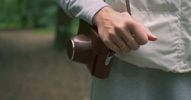 Vrouwelijke hand holdinga camera in een bruine geval op haar schouder in bos in het voorjaar — Stockvideo