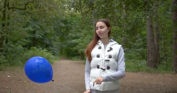 Щаслива дівчина стоїть з блакитною кулею і посміхається в лісі в шлю-мо — стокове відео