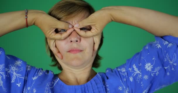 Frau lächelt und macht eine Geste der Finger in Form einer Brille auf ihrem Gesicht — Stockvideo