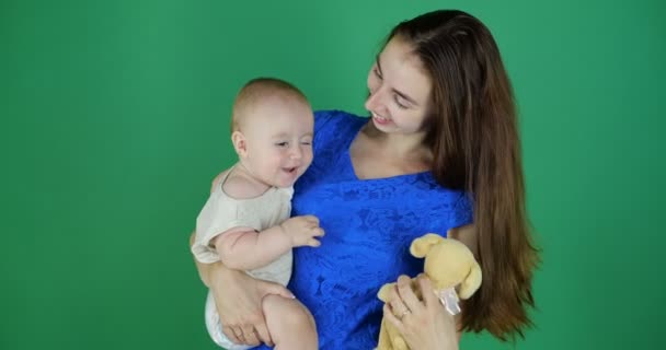 4k-een jonge moeder houdt een schattige peuter op een groene achtergrond in de Studio — Stockvideo
