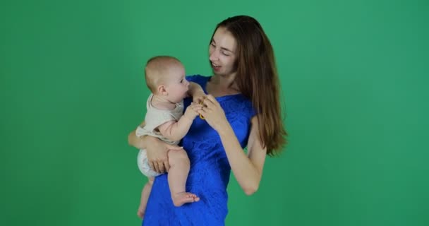 4K-ένα νεαρό κορίτσι κρατά ένα χαριτωμένο νήπιο σε ένα πράσινο φόντο στο στούντιο — Αρχείο Βίντεο