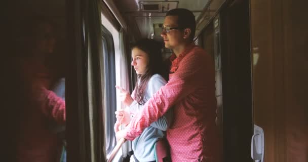 Jovem e sua esposa feliz olham para fora de uma janela de trem em câmera lenta — Vídeo de Stock