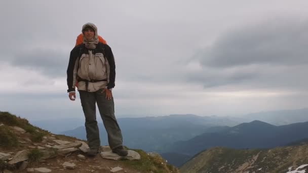 Valiente turista con una mochila agitando su mano en la cima de una montaña en slo-mo — Vídeo de stock