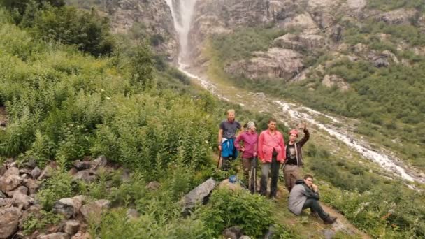 4k - Expedición de turistas jóvenes saludando cerca de la cascada de montaña, acción aérea — Vídeo de stock