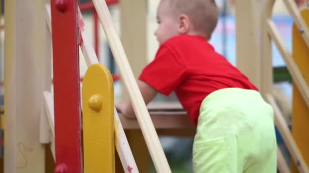 Un niño pequeño está subiendo a un tobogán en el patio de recreo en cámara lenta — Vídeos de Stock