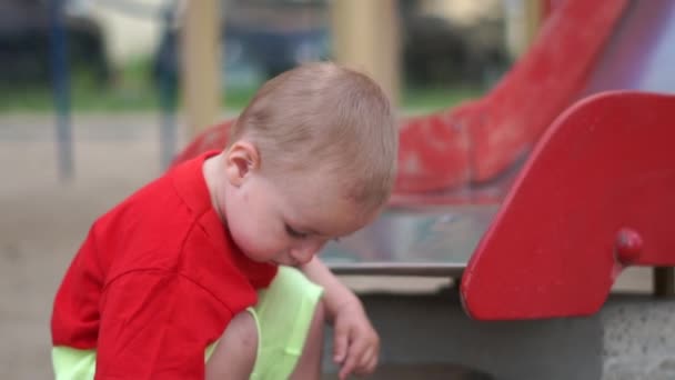 Il bambino si accovaccia vicino allo scivolo nel parco giochi e gioca al rallentatore — Video Stock