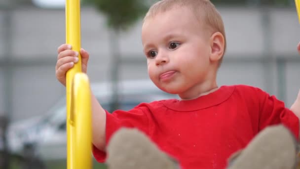 Little boy riding on a swing on the playground on a summer day in slow motion — Stock Video