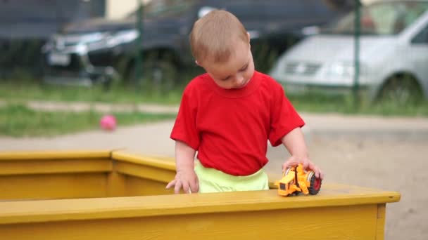 A little boy is standing in the sandbox, playing with a broken car, slow motion — Stock Video