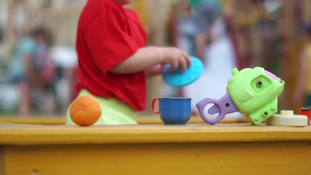 Een peuter spelen met speelgoed in de zandbak op de speelplaats in slow motion — Stockvideo