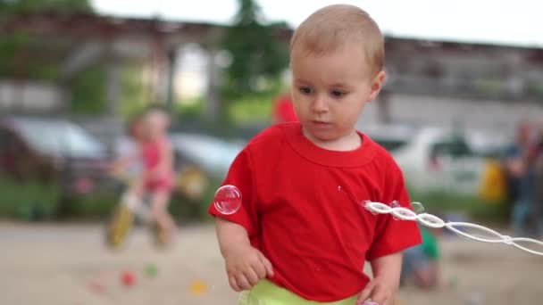 Roztomilá chlapeček běží a chytá na hřišti mýdlové bubliny v pomalém pohybu — Stock video