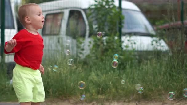 Маленький мальчик ловит мыльные пузыри на фоне размытых машин, замедленной съемки — стоковое видео