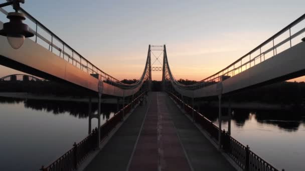 Tiro aéreo de uma ponte suspensa mágica sobre o Dnipro ao pôr-do-sol vermelho e roxo — Vídeo de Stock