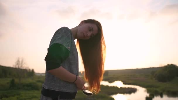 Güzel kız yavaş çekimde gün batımında doğa üzerinde uzun kırmızı saç fırçalar — Stok video