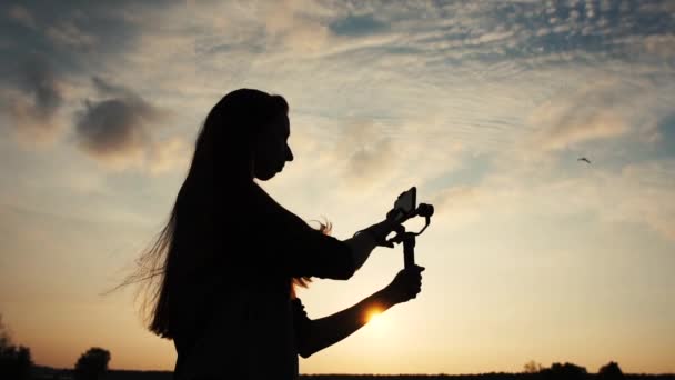 Silhouet van een meisje met smartphone op de stabilisator in haar handen, Slow Motion — Stockvideo