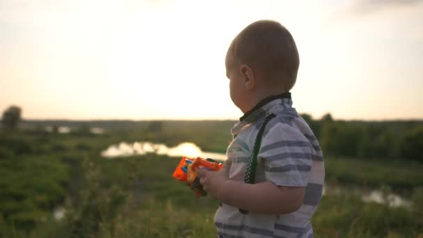 Um menino bonito e elegante brinca com um trator ao pôr do sol em câmera lenta — Vídeo de Stock