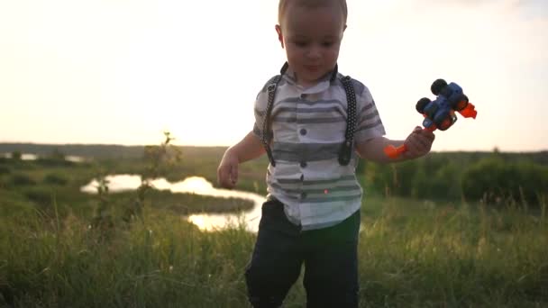 Un niño lindo juega con un tractor en la naturaleza al atardecer en cámara lenta — Vídeos de Stock