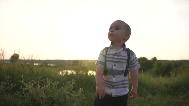 Un lindo niño pequeño con una camisa elegante golpea la pelota al aire libre en cámara lenta — Vídeo de stock