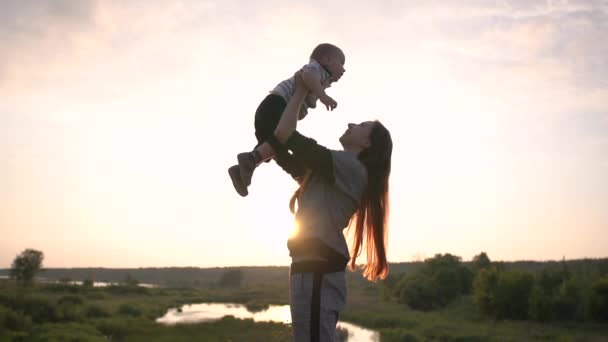 Vrolijk meisje gooit omhoog en kusjes haar zoon, staande op de weide in slow motion — Stockvideo